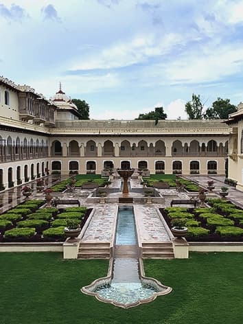 Rambagh Palace gardens at evening, formal lawn with brass diyas and silk canopies