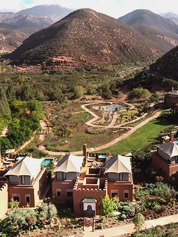 Kasbah Tamadot terrace at dusk, lantern-lit ramparts against mountain ridge